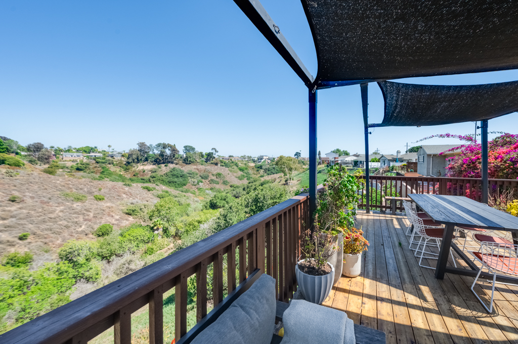 Wood deck with shade sails and an outdoor dining table overlooking a canyon in Clairemont, with homes along the far rim.