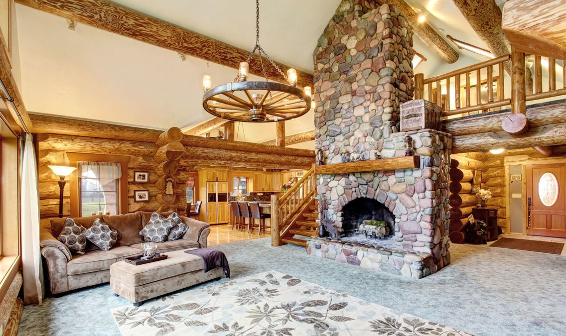 Bright Living room interior in American log cabin house. Rustic chandelier, stone fireplace and high ceiling