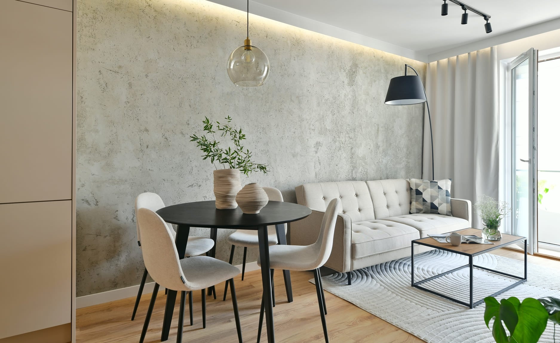 Loft living room with beige sofa, black arc lamp, dining area with black round table in a modern apartment with architectural concrete wall background and led light illumination
