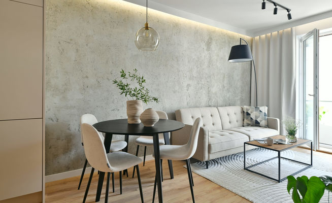 Loft living room with beige sofa, black arc lamp, dining area with black round table in a modern apartment with architectural concrete wall background and led light illumination (1)