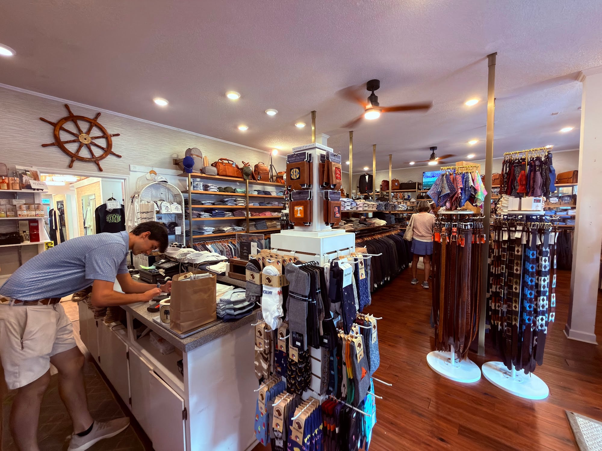Checkout counter and accessory displays inside the Pawleys Island Men's Store, with a ship's wheel overhead