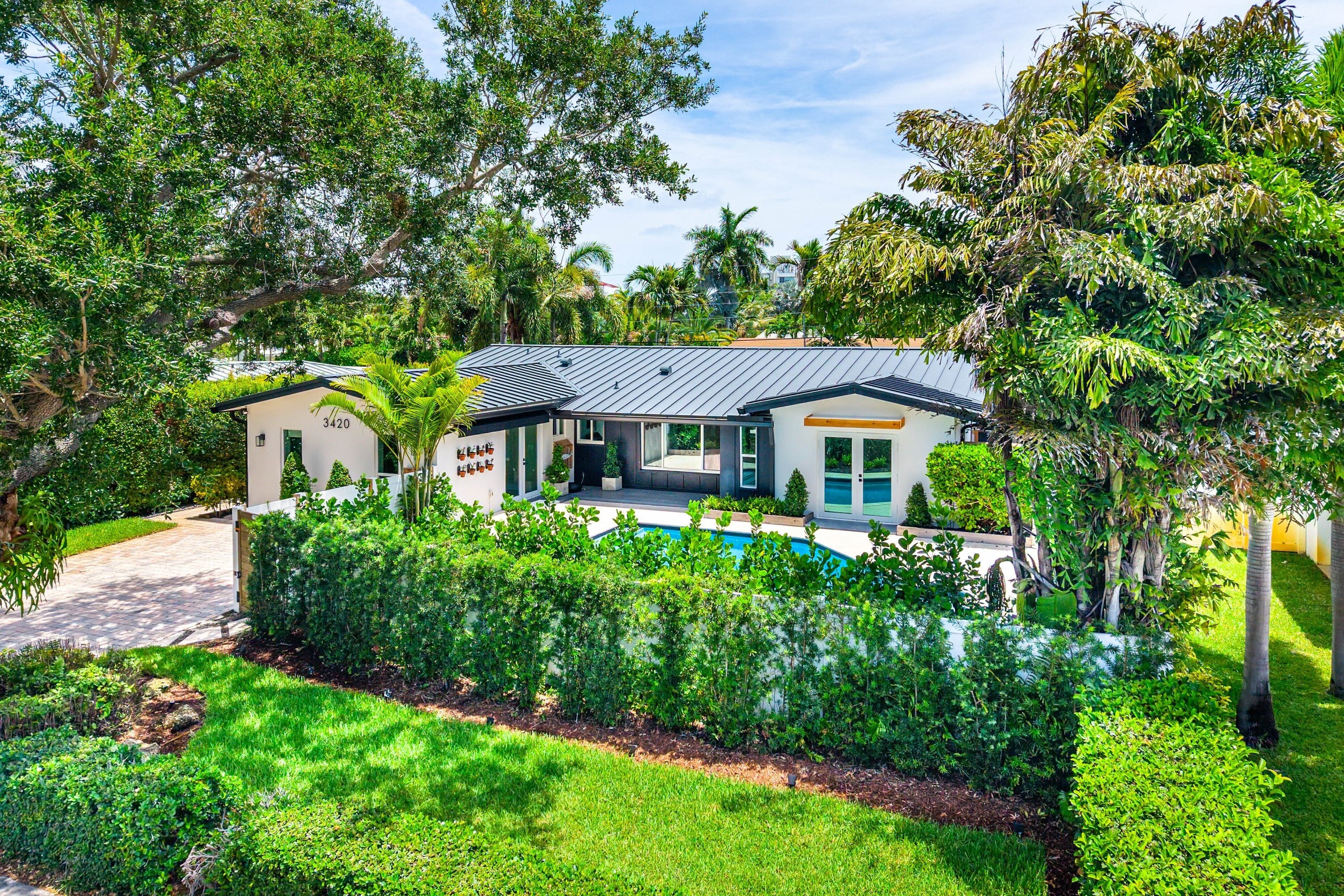 Coral Terrace pool home at 3420 NE 17th Terrace Oakland Park FL featuring a standing seam metal roof paver driveway and tropical landscaping