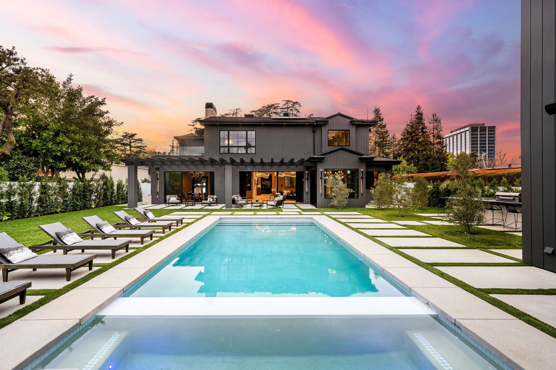A luxurious modern house with a swimming pool in the backyard, surrounded by greenery and a beautiful sunset sky.