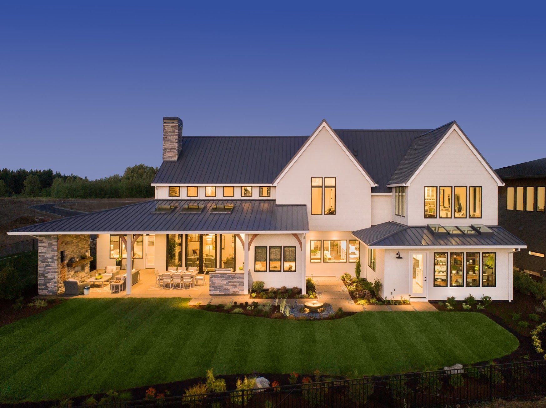 Luxury Home Exterior at Night Beautiful New House with Large Yard, Outdoor Covered Patio with Kitchen, and Glowing Interior Lights