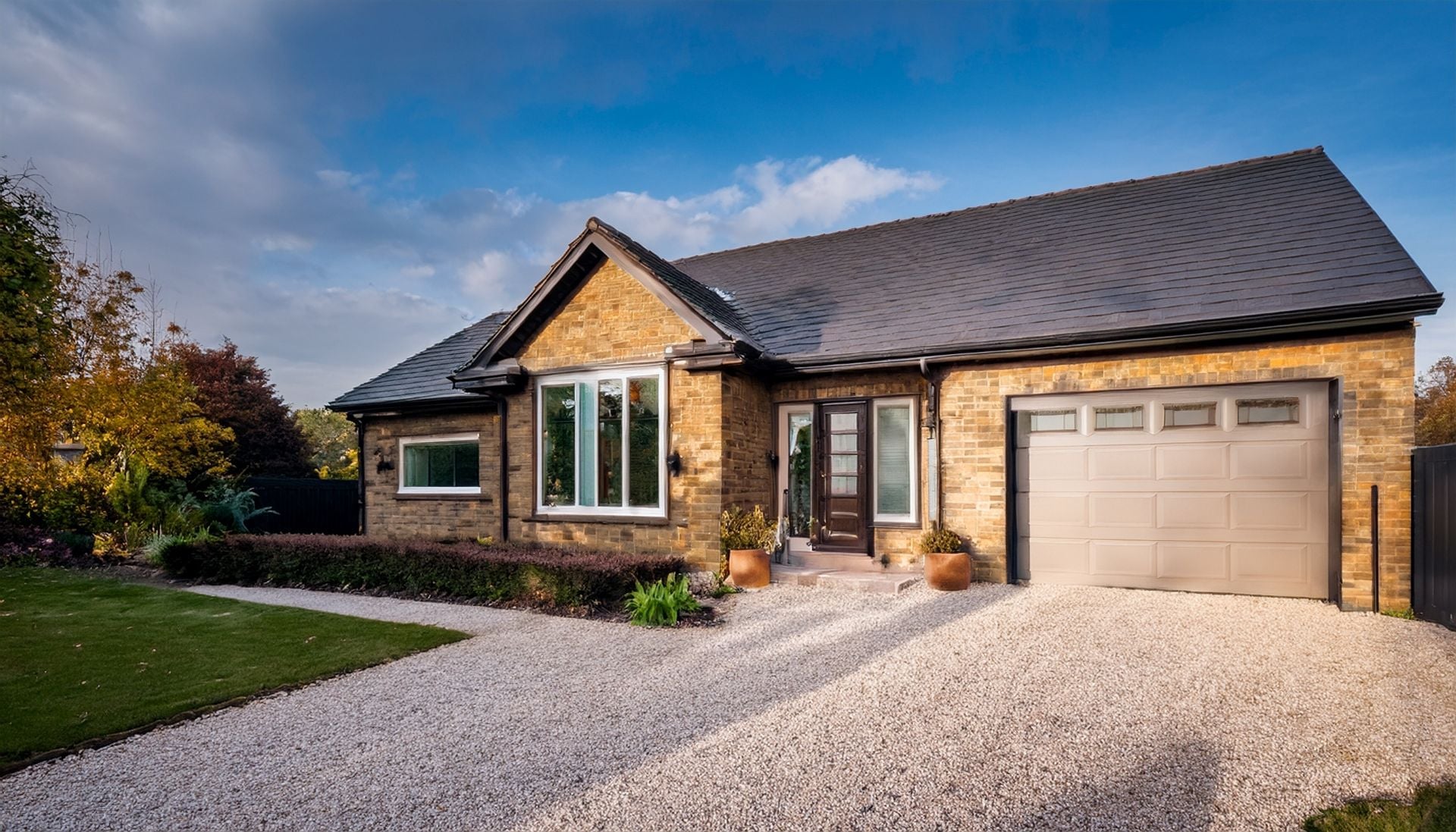 Modern ranch house with brick exterior, attached garage, and gravel driveway. Autumn landscaping.