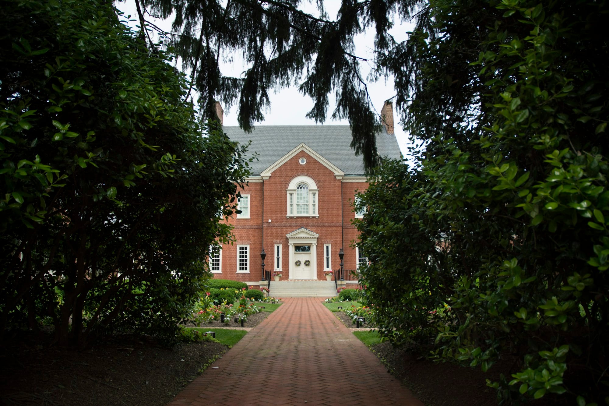 Georgian-style red brick home framed by mature trees and a brick walk
