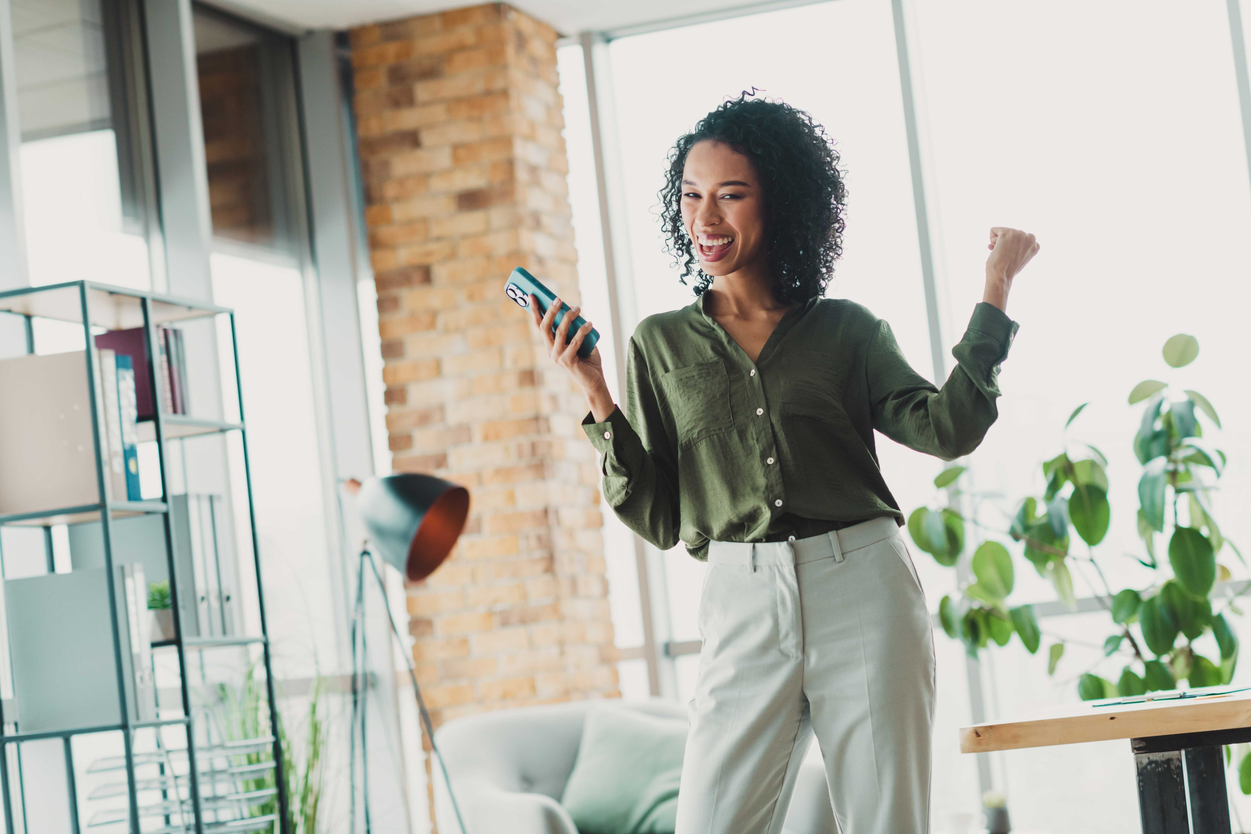 Young professional celebrating success in a bright modern office space while looking at her smartphone with excitement