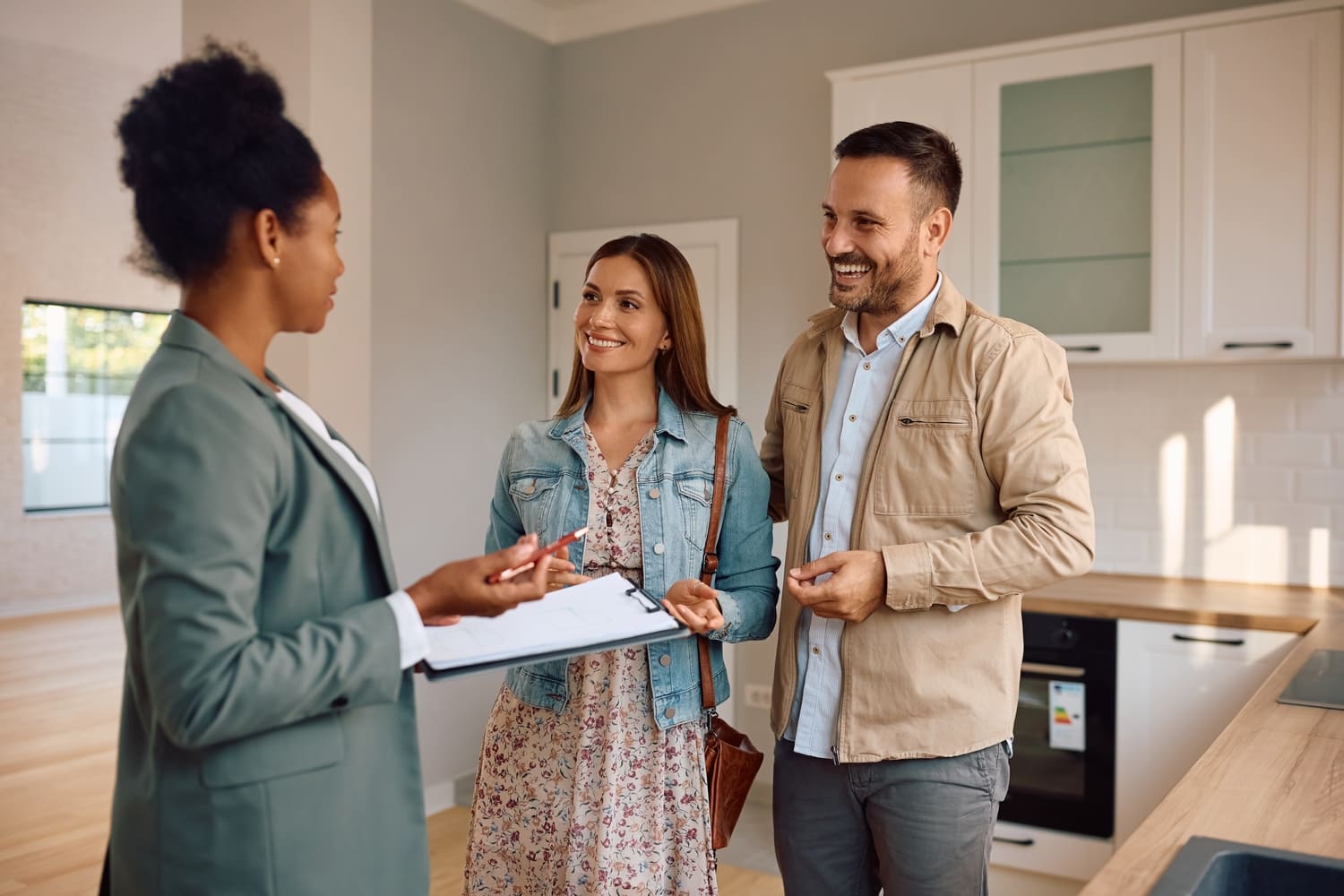 Happy couple of real estate buyers and their agent talking in the kitchen during open house day. (1) (1)