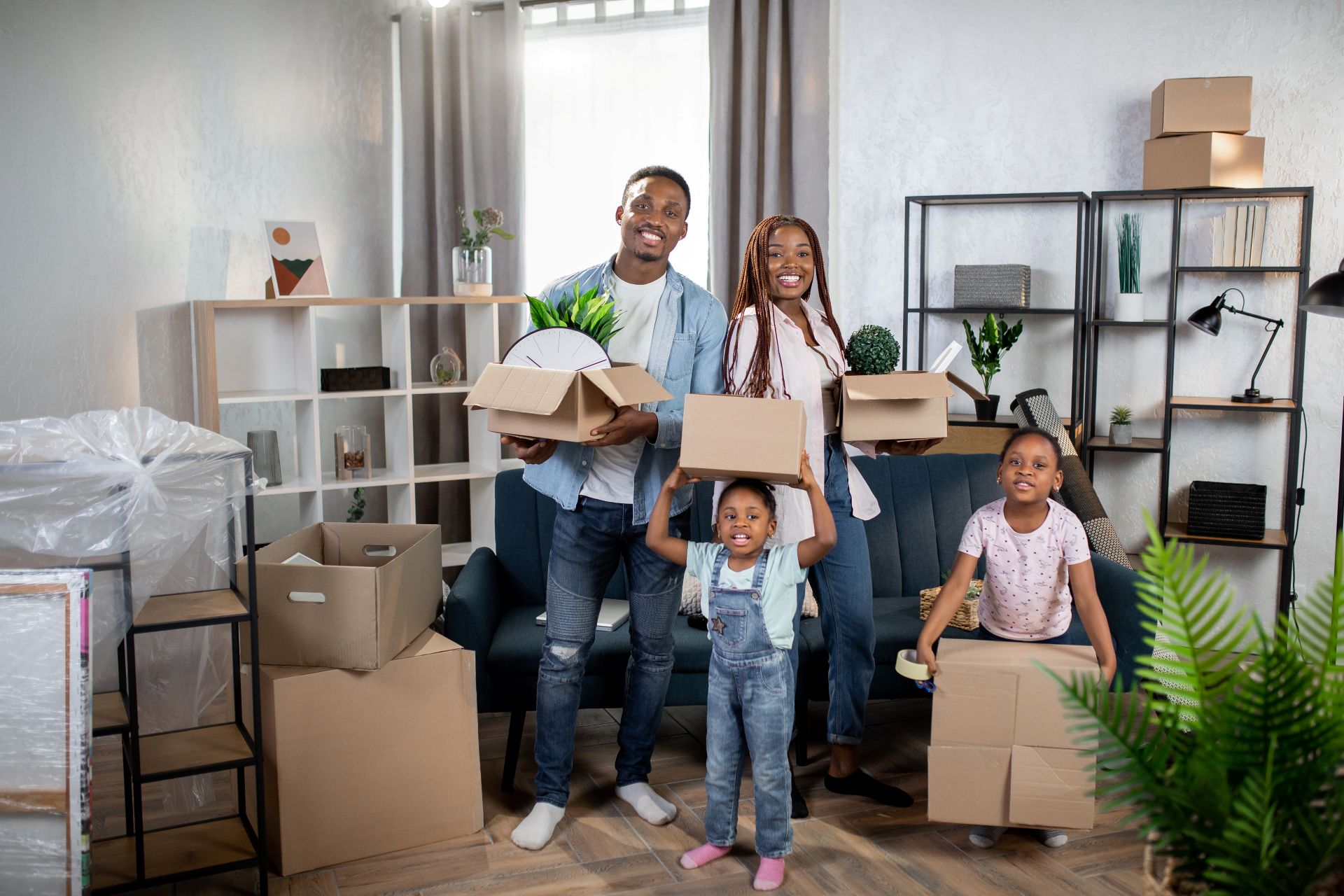 Cheerful afro american family holding boxes while standing at bright modern apartment.