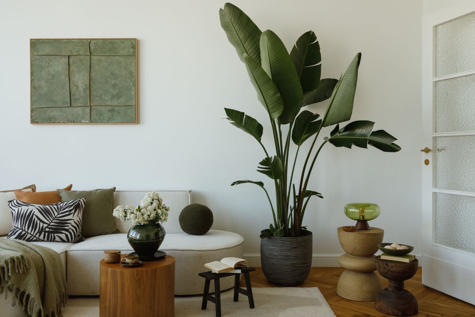 Comfortable interior with tropical plant, round wooden coffee tables and minimalist furniture setup. Mock up art on the wall.