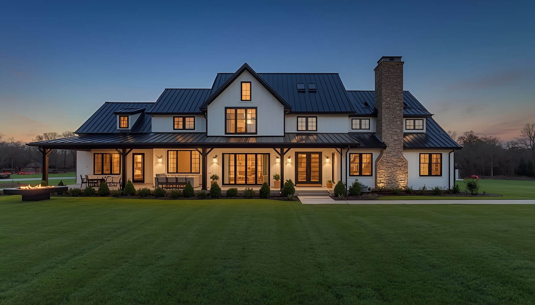 Luxurious white farmhouse exterior dusk lighting architectural design metal roof fire pit backyard lawn suburban home dream house evening real estate