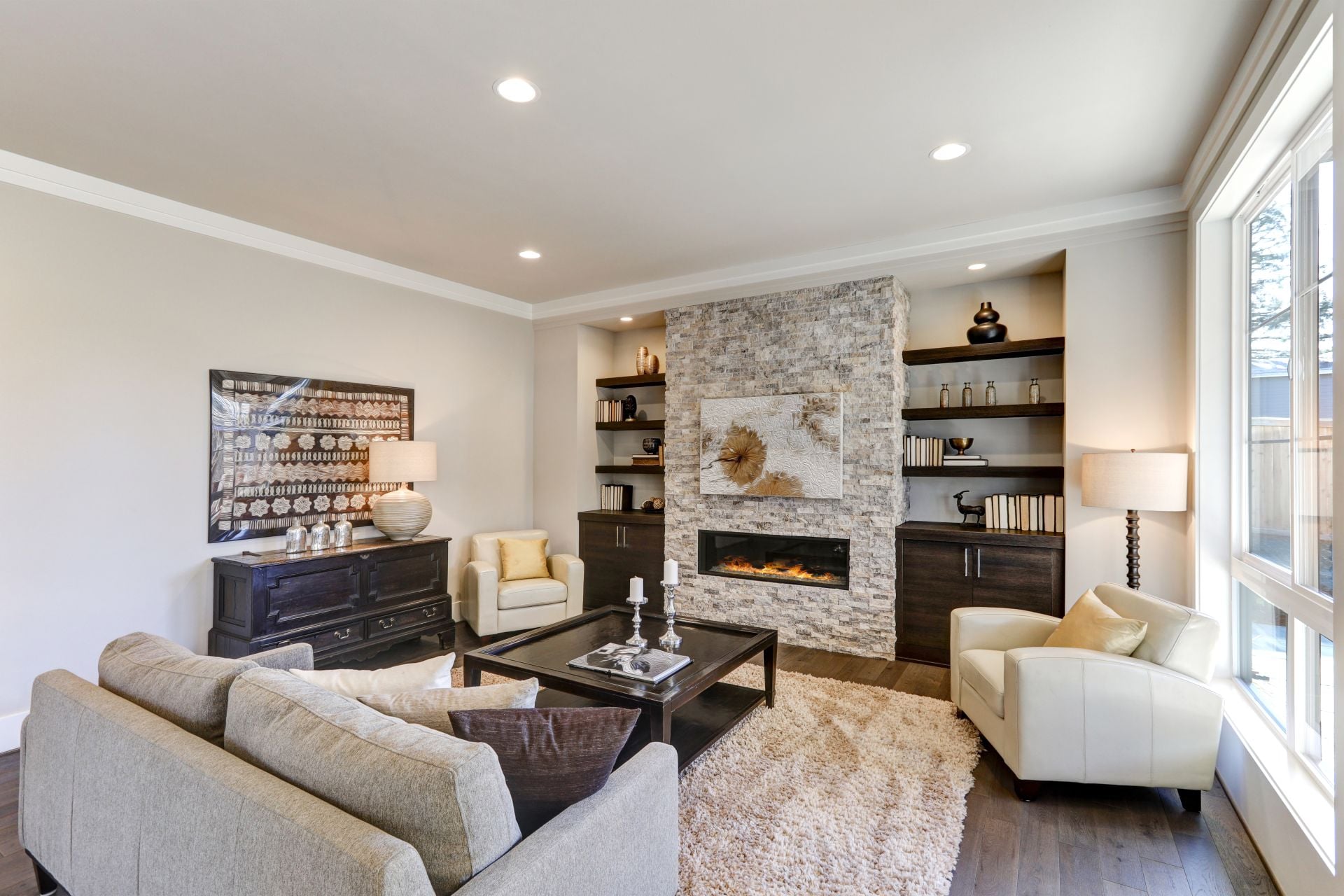 Living room interior in gray and brown colors features gray sofa atop dark hardwood floors facing stone fireplace with built-in shelves. Northwest, USA