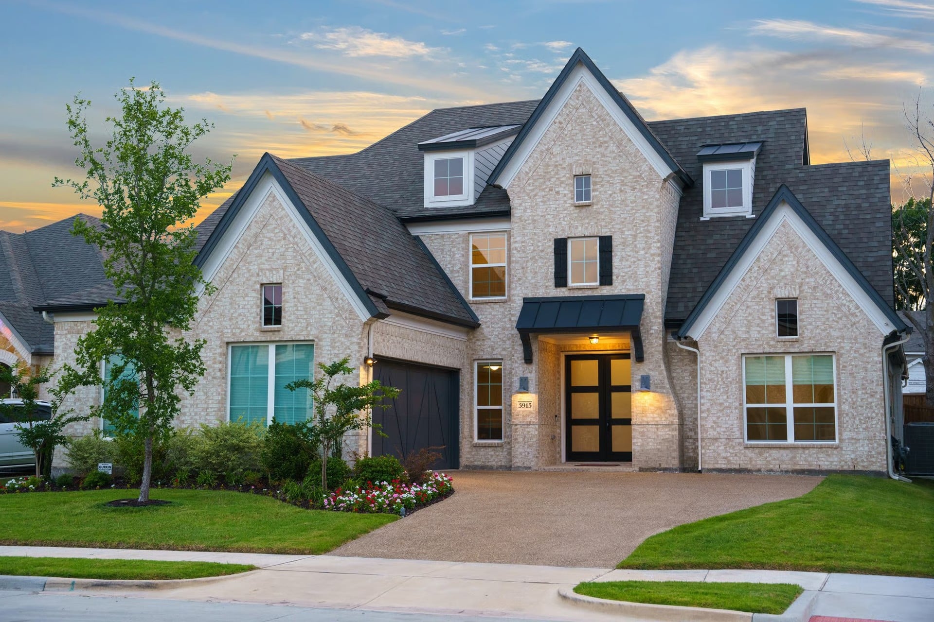 Two-story brick and stone home with lit entryway in a Rowlett, TX neighborhood at dusk