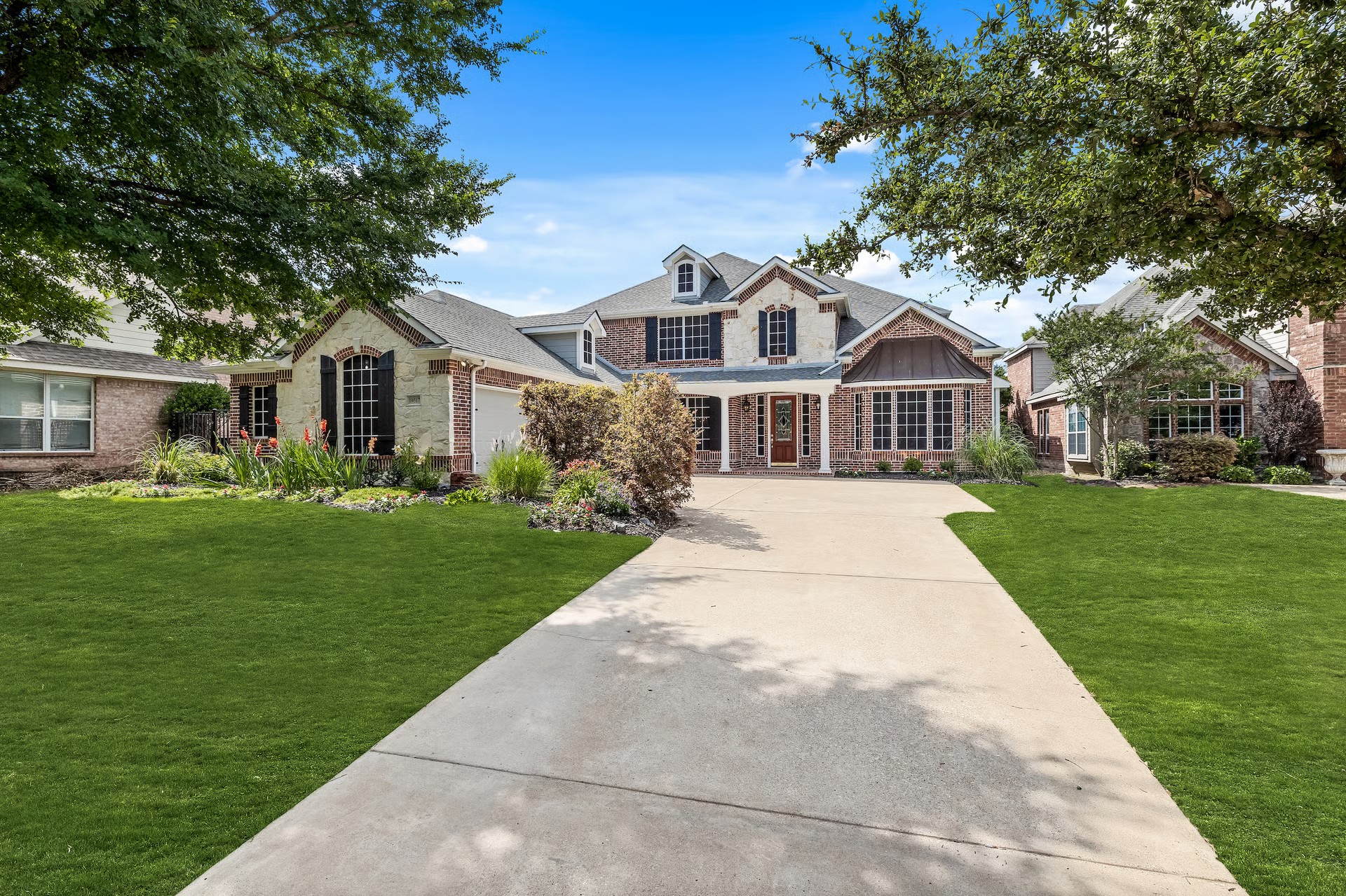 Two-story brick and stone home in Waterview with mature trees and a long circular driveway