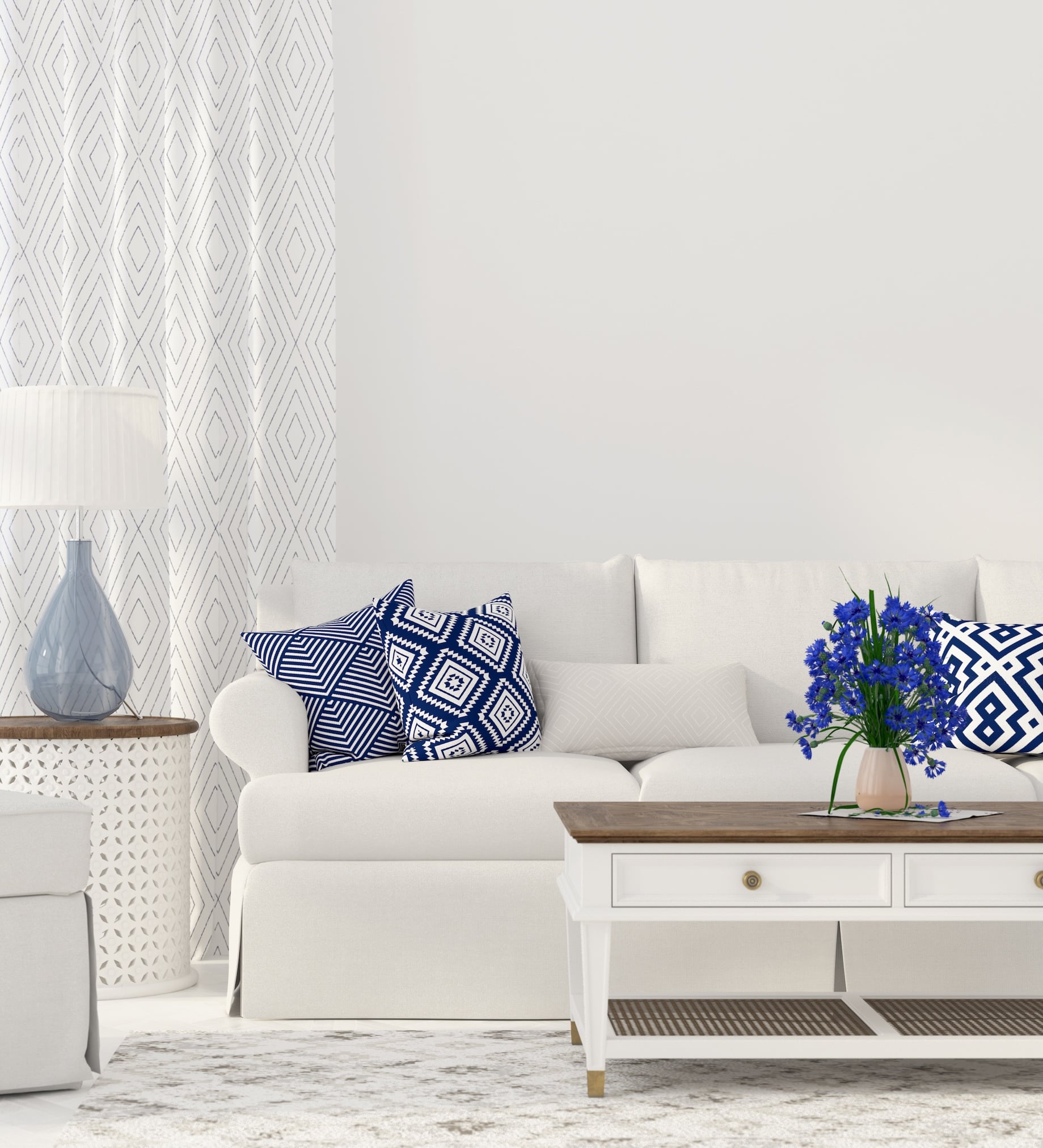 Bright living room with a white sofa, navy and white patterned pillows, a white coffee table, and blue cornflowers in a vase