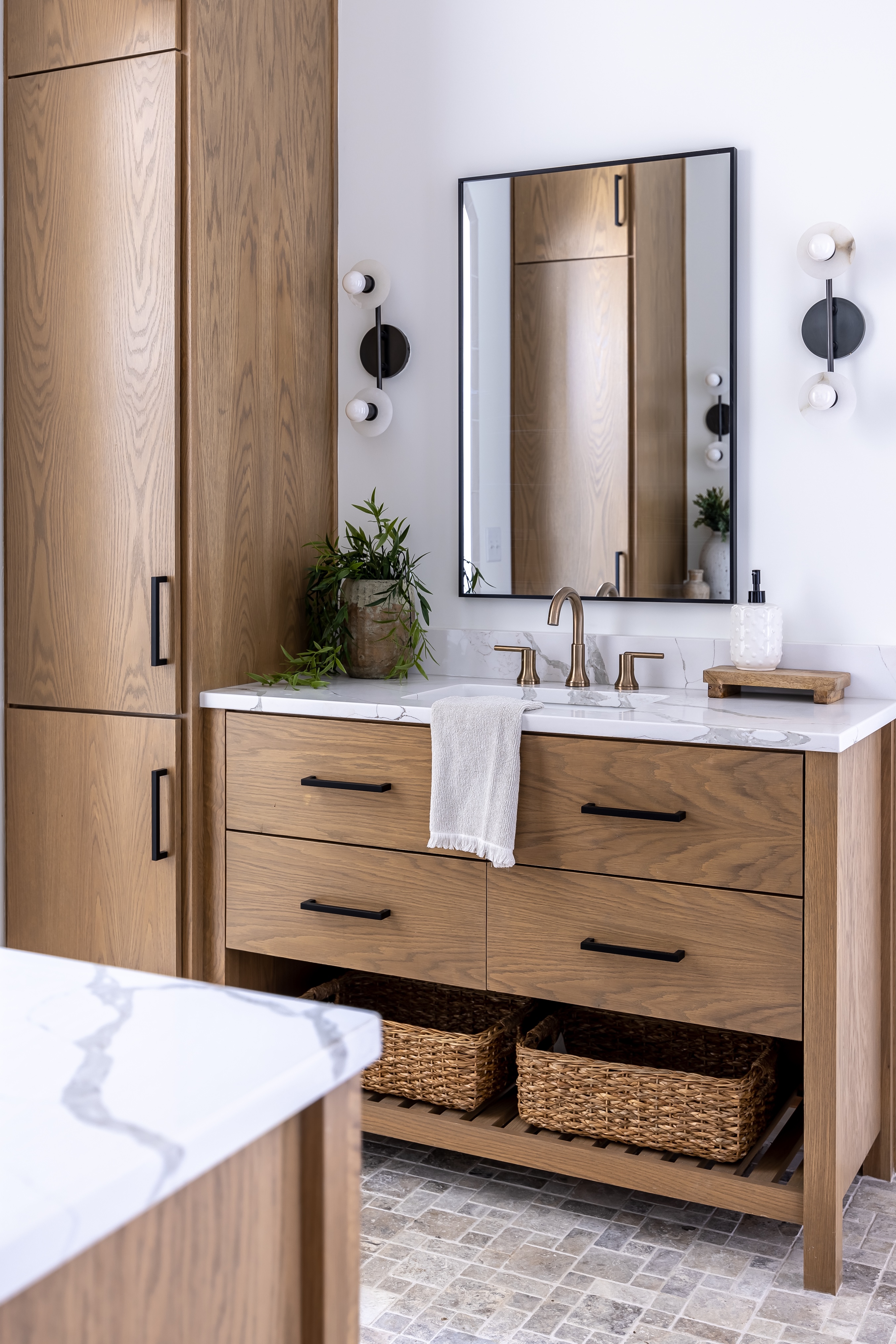 Renovated bathroom with a white oak vanity, quartz countertop, undermount sink, framed mirror, wall sconces, and stone tile flooring.