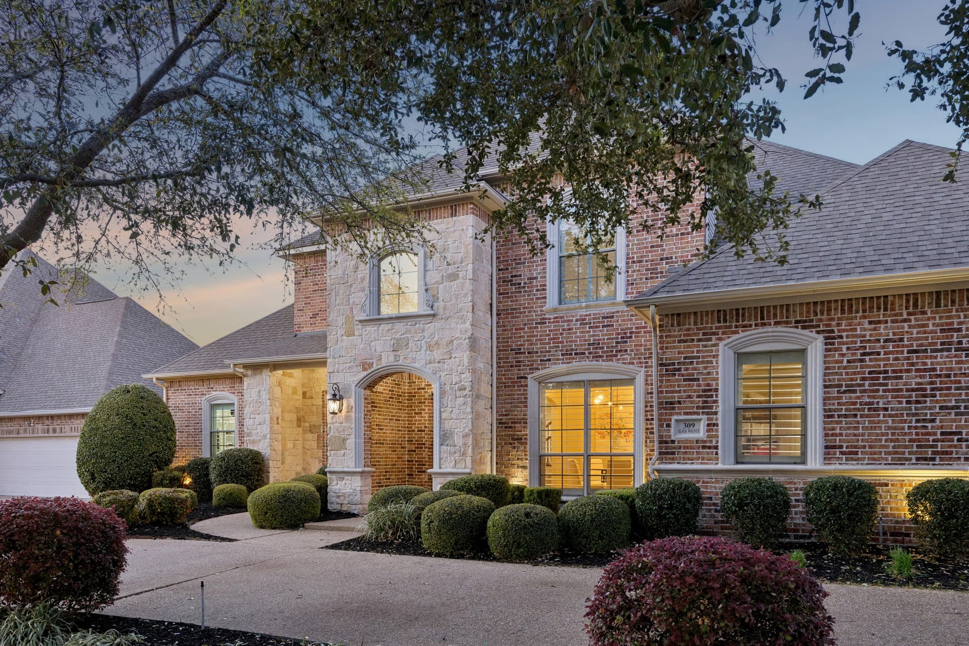 Two-story brick and stone custom home at dusk with arched entry, 309 Black Walnut, Garland TX