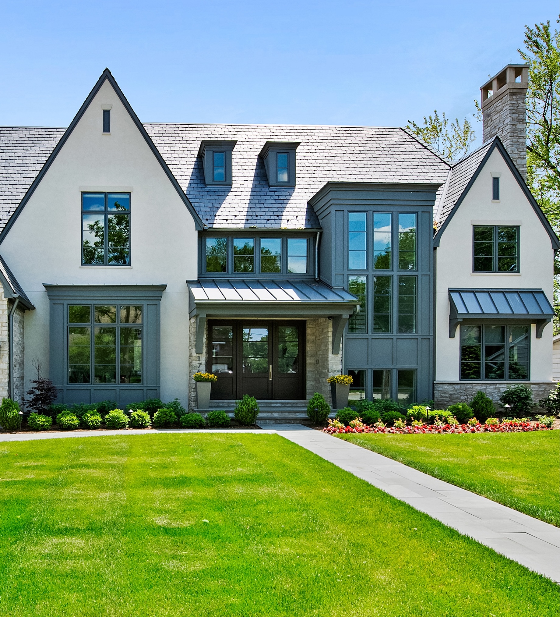 Large two-story stone and stucco home with steep gables, a stone chimney, and manicured landscaping along a curved stone walkway