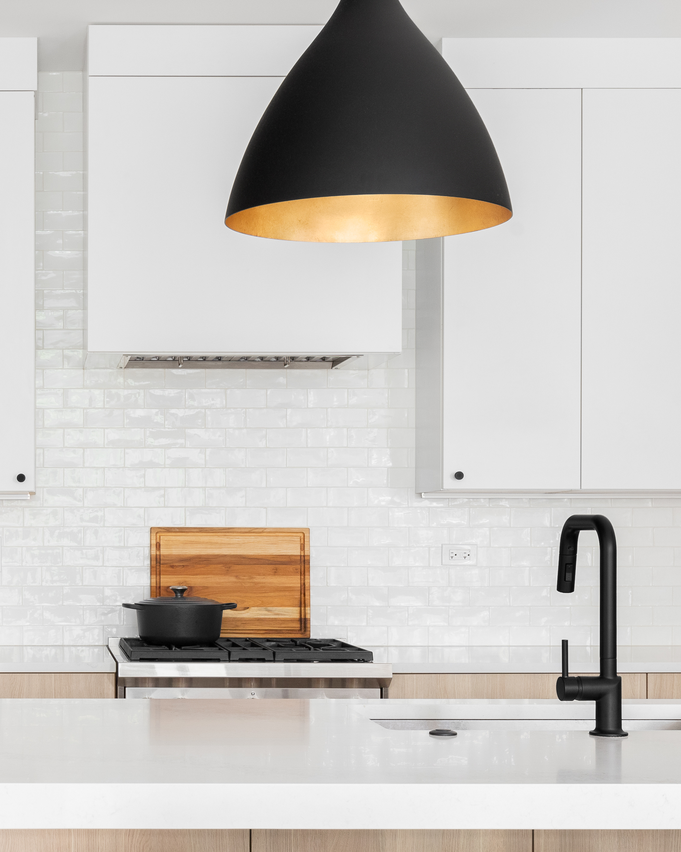 Modern kitchen with white subway tile backsplash, light oak cabinetry, a quartz island, and a matte black pendant light above a gas cooktop.