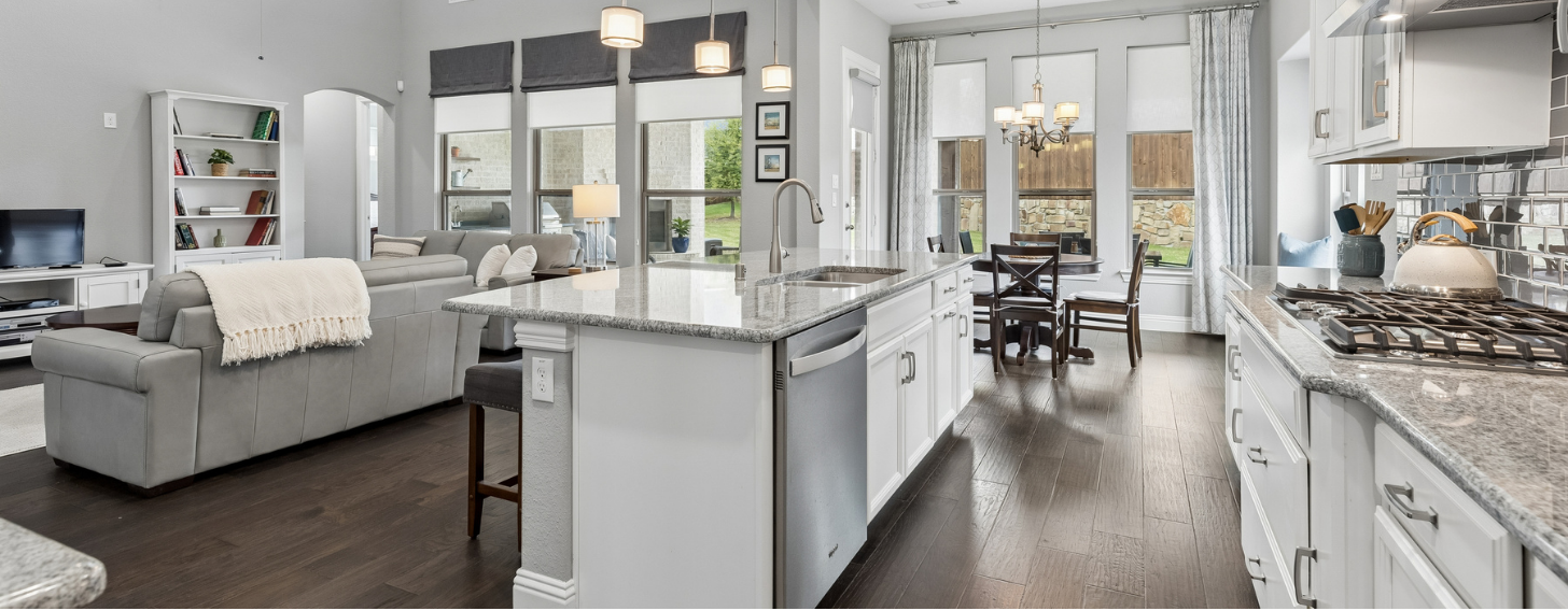 Open-concept kitchen with white cabinets, granite island, and hardwood floors opening to a living area
