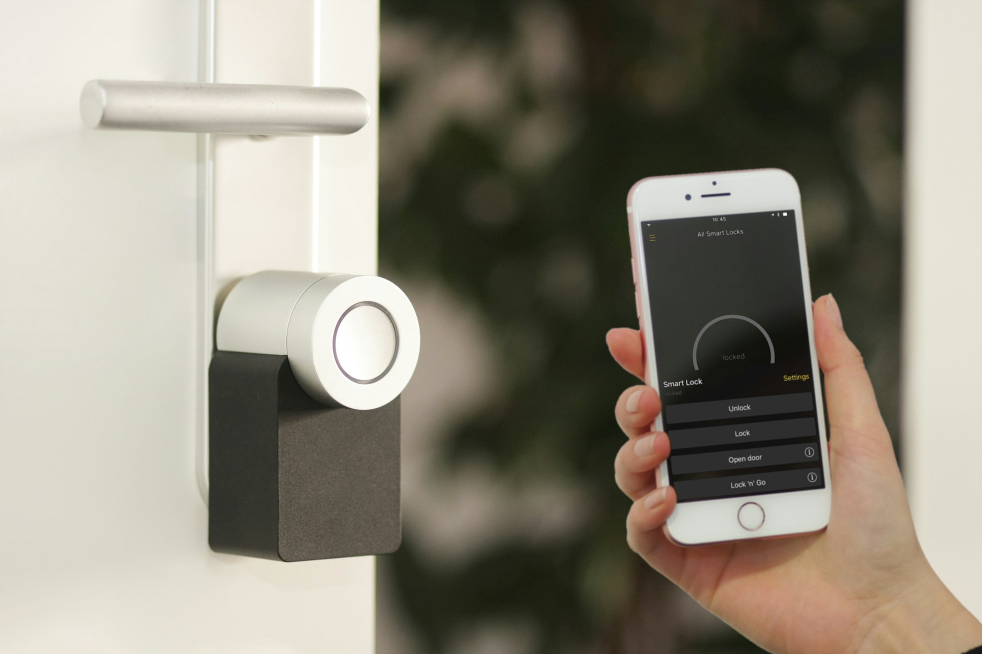 Hand holding a smartphone with a smart lock app next to a keyless entry door lock