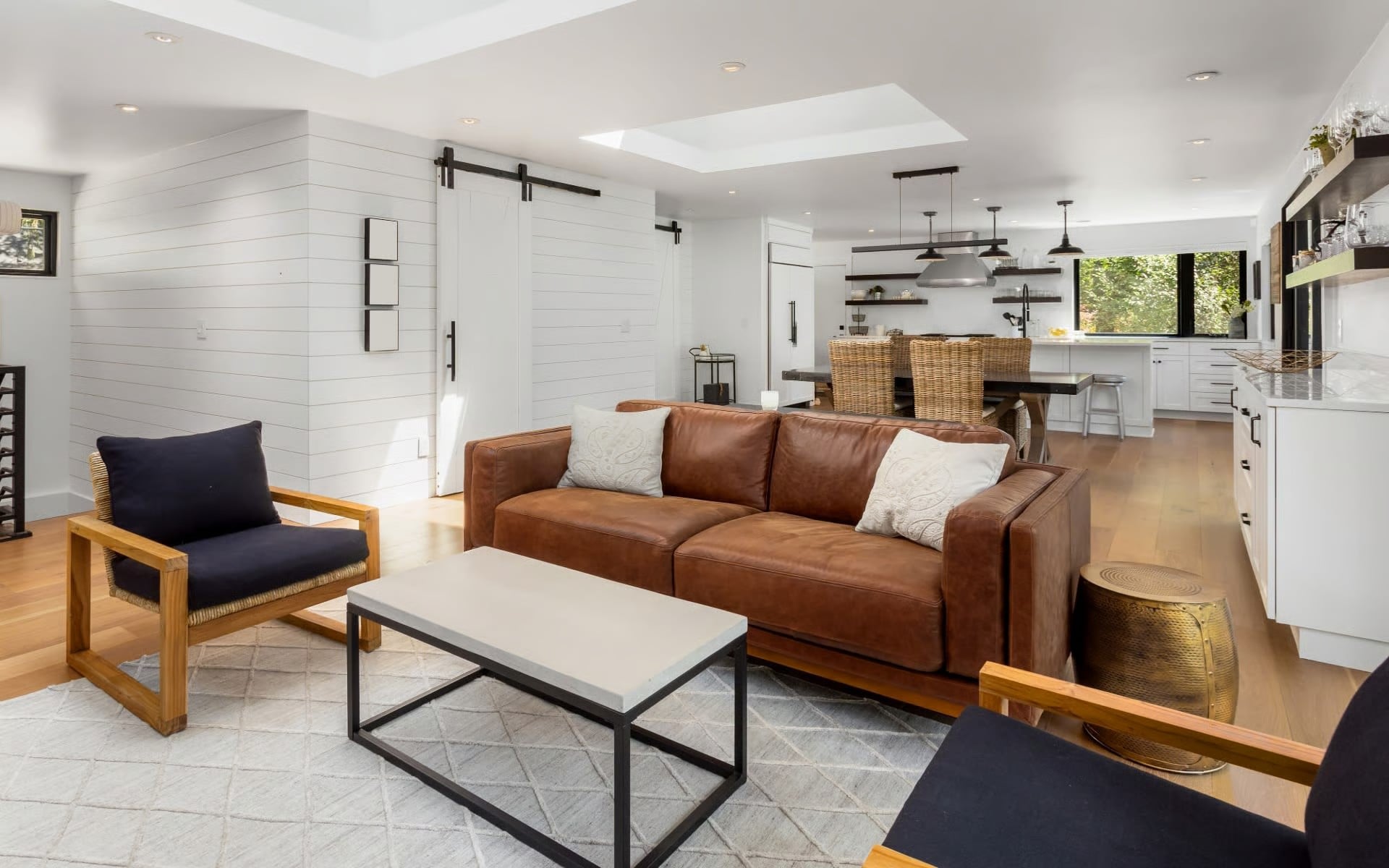 Open-concept living room with a leather sofa, shiplap accent wall, and kitchen visible in the background