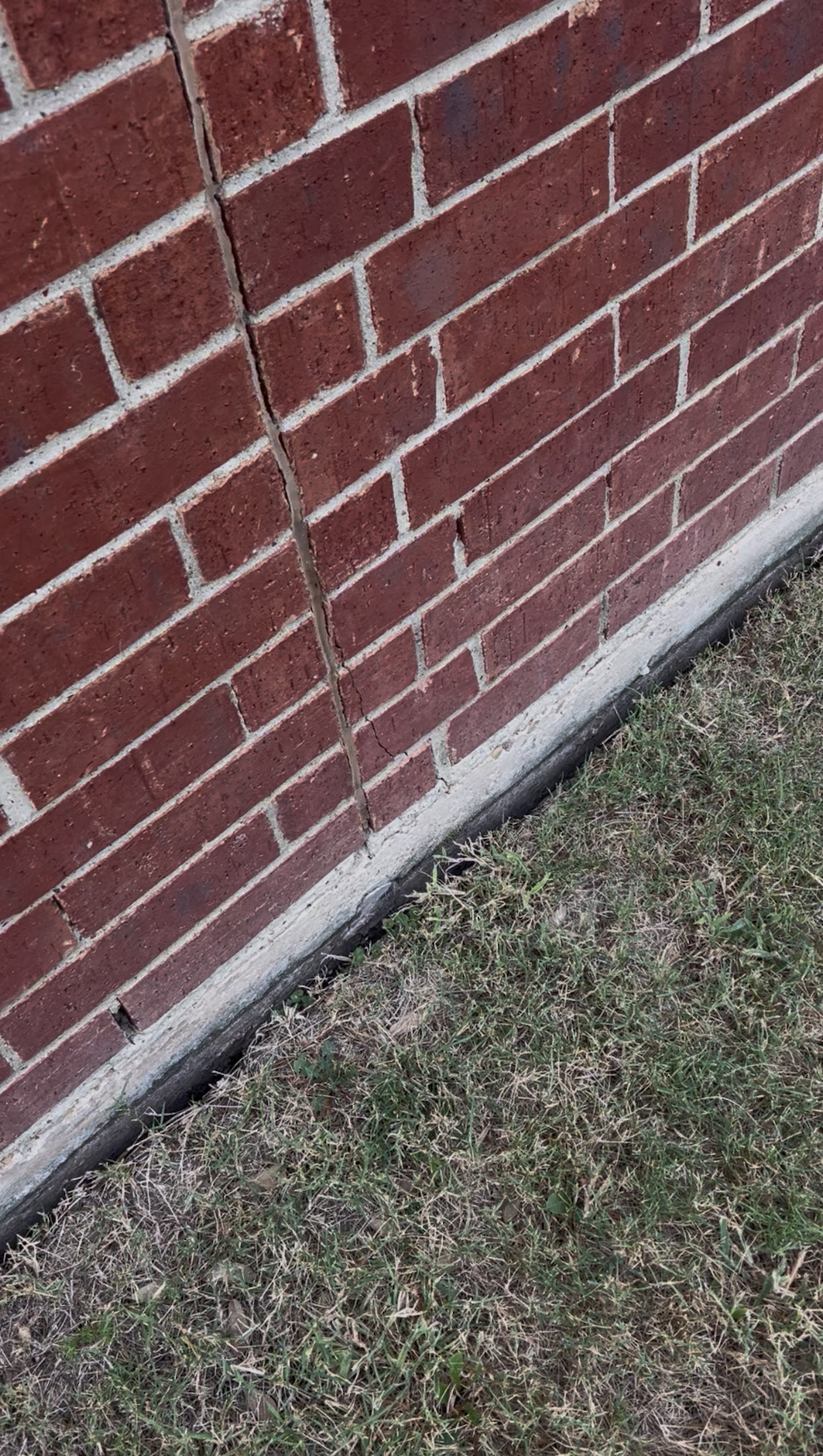 A visible gap between dry soil and the concrete slab edge along the brick exterior of a home.