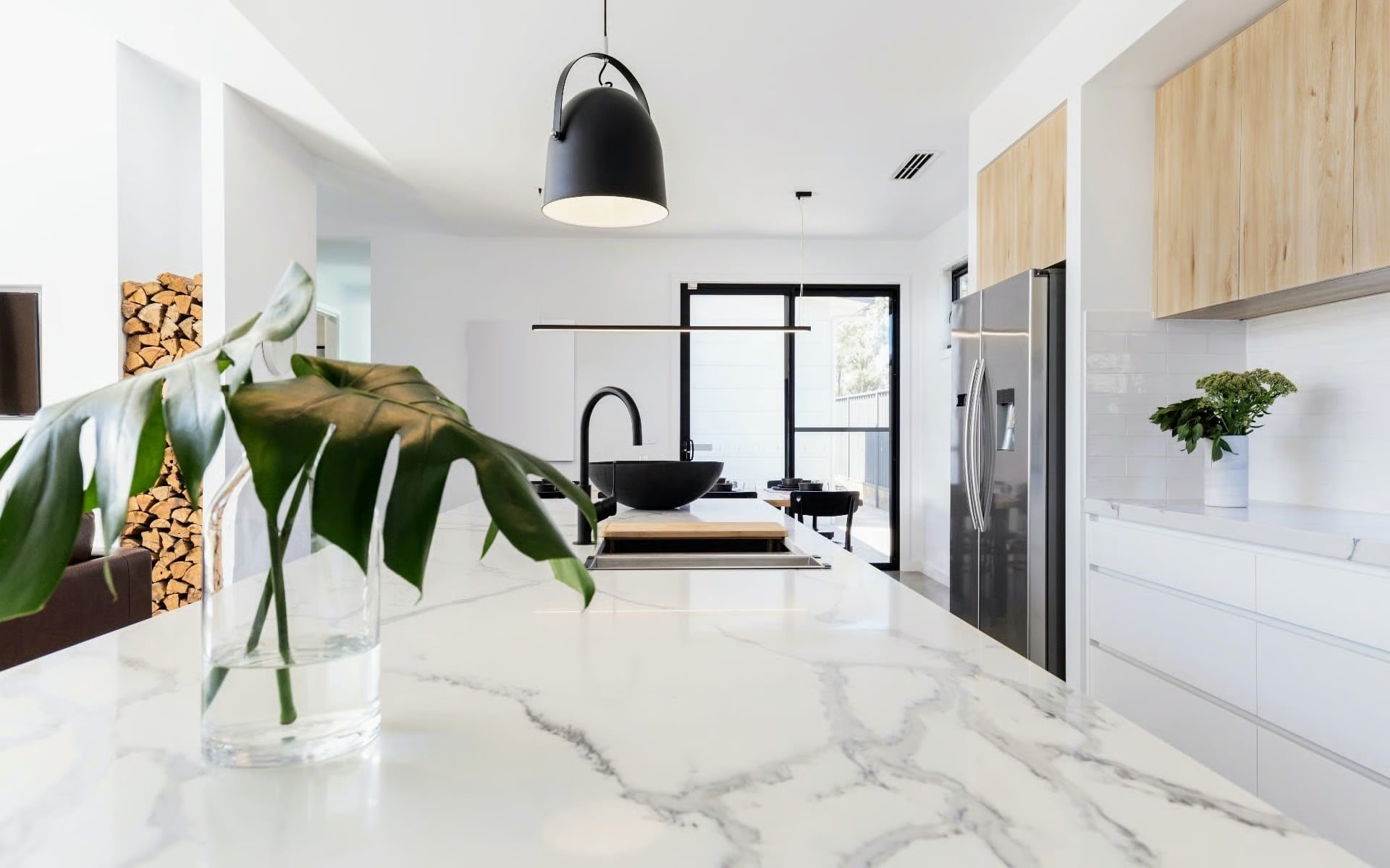 Modern white kitchen with marble island, black fixtures, and stainless refrigerator