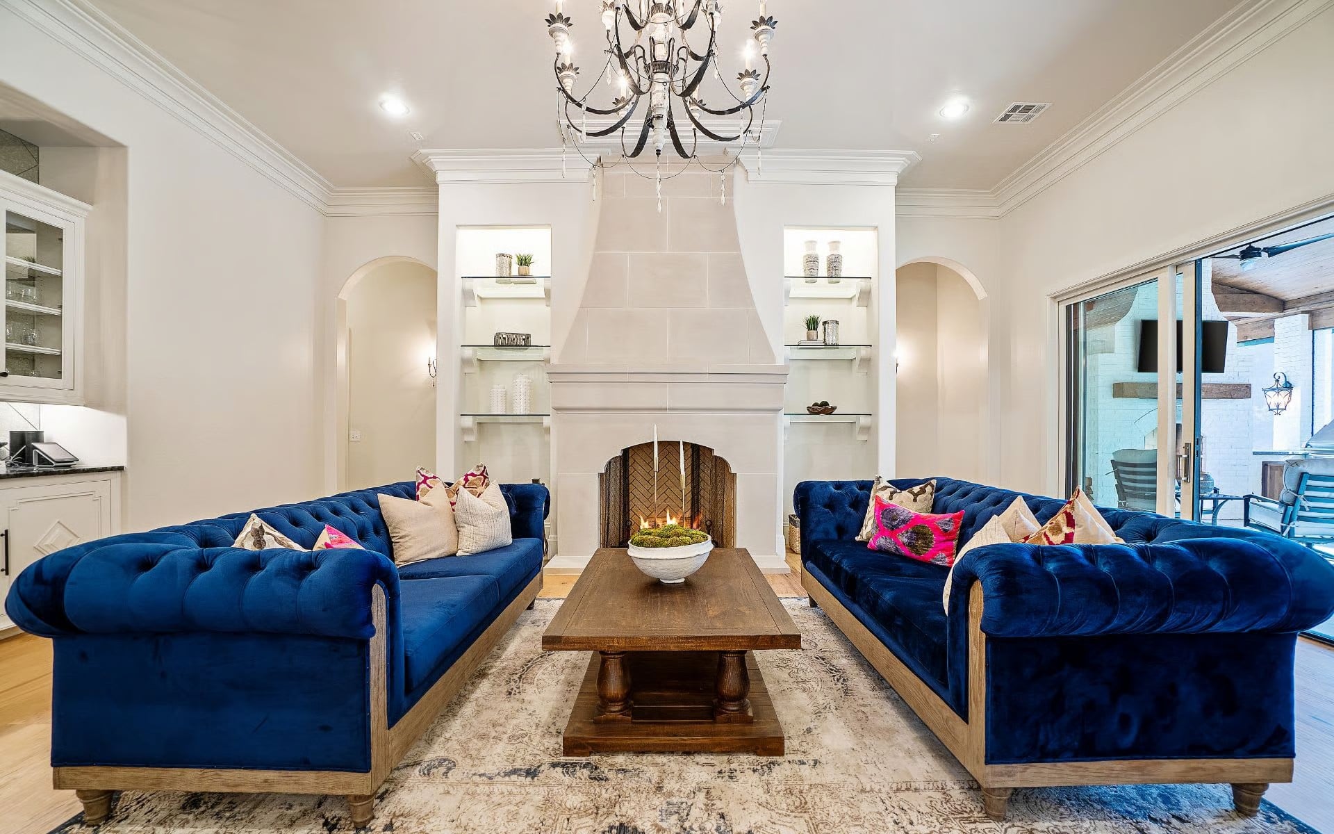 Formal living room with two navy velvet sofas facing a stone fireplace and crystal chandelier