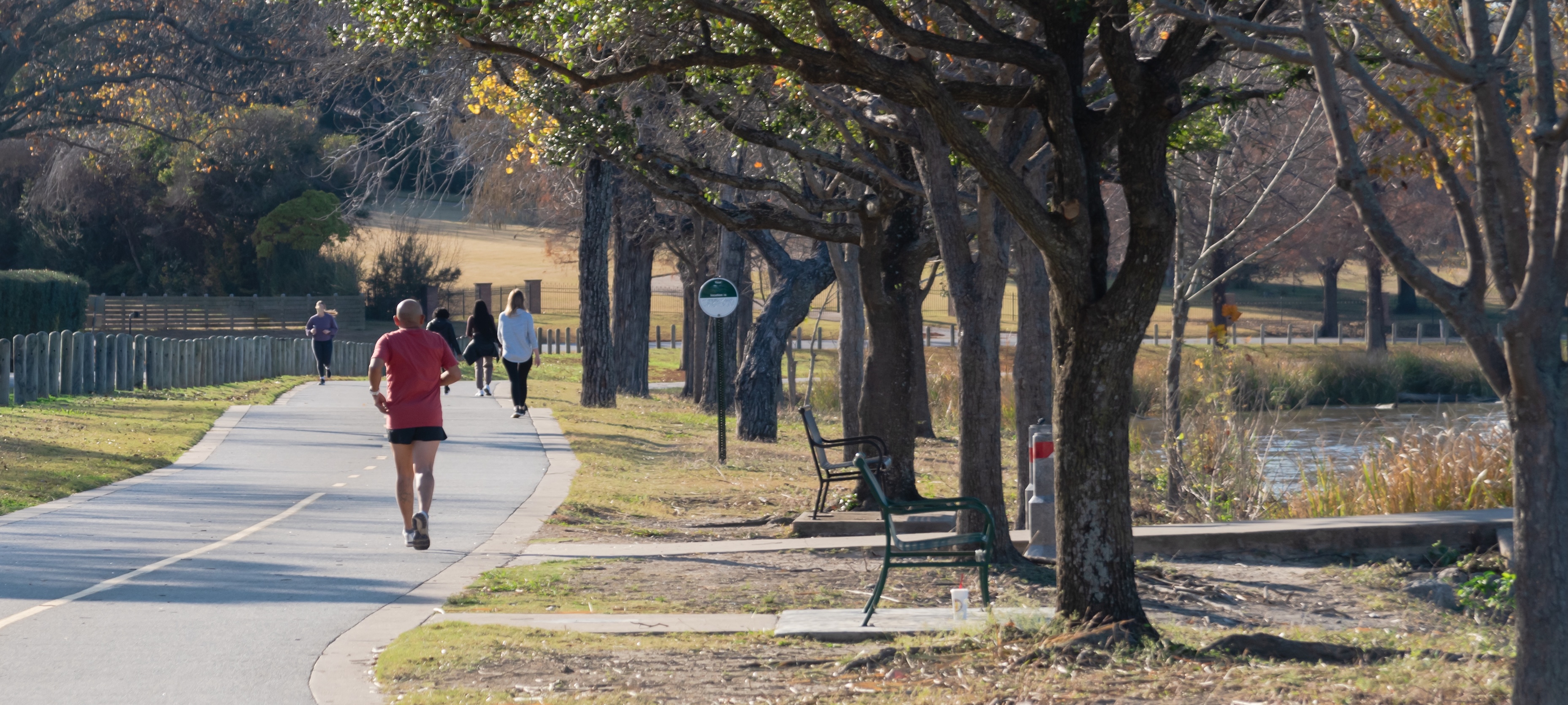 Joggers, walkers, and cyclists enjoying a tree-lined paved trail beside White Rock Lake in Dallas, Texas, near Lake Highlands.