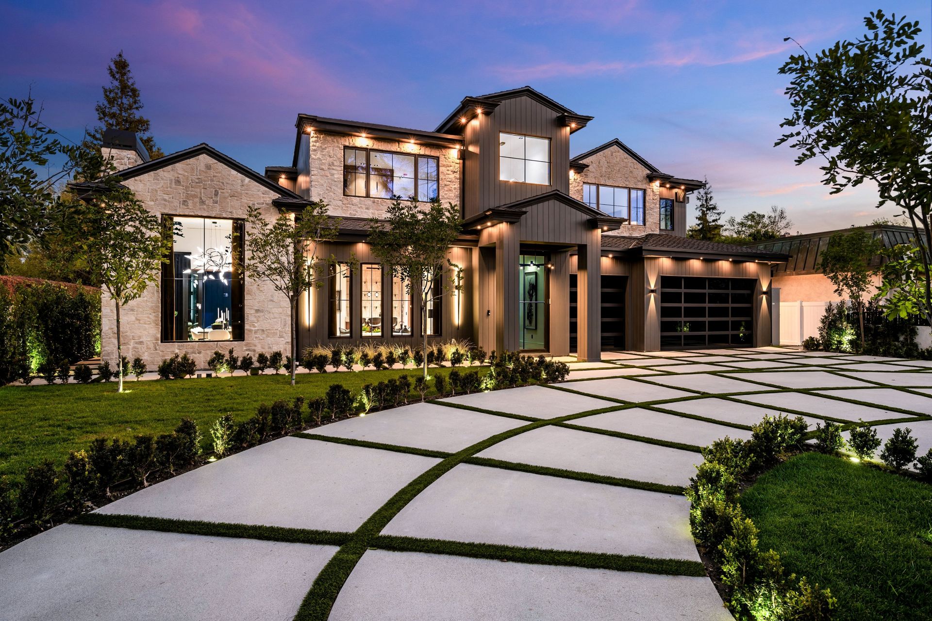 Modern luxury home exterior with a beautifully landscaped front yard and driveway at dusk.