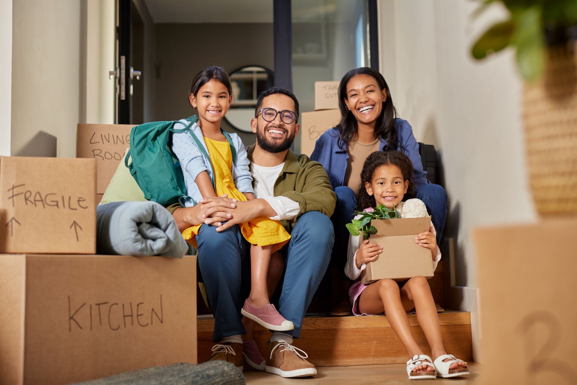 Middle eastern family sitting on stairs surrounded by moving boxes. Indian parents and their two daughters smiling on moving day.