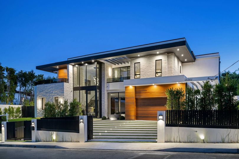Modern luxury house exterior with large windows, landscaped yard, and evening lighting.