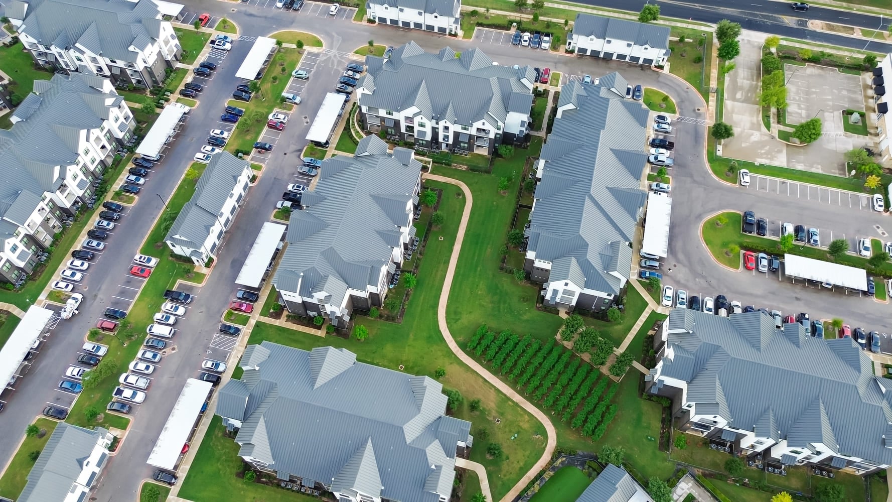 New development suburban farmhouses style apartment complex metal roofing, busy outdoor parking lot in Pflugerville, fast-growing city suburbs of North Austin, Travis County, Texas, aerial view. USA
