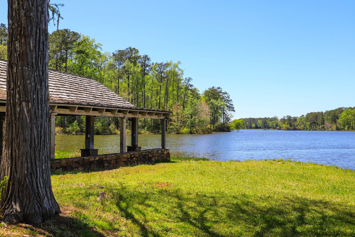 a brown wooden boat house on a gorgeous vast blue lakes surrounded by lush green trees, grass and plants with blue sky at Callaway Gardens in Pine Mountain Georgia USA