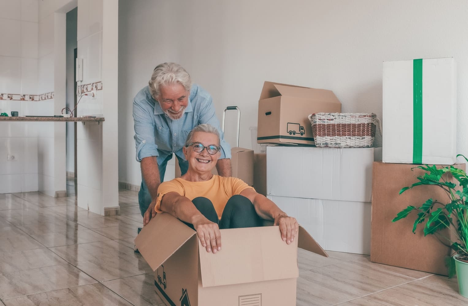 A playful older couple moves into a new home, surrounded by moving boxes in an empty room. A concept of a fresh start, retirement, and relocation.