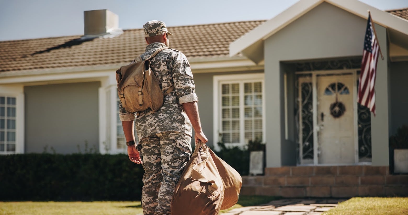 Patriotic young soldier walking towards his house with his luggage. Rearview of an American serviceman coming back home after serving in the military