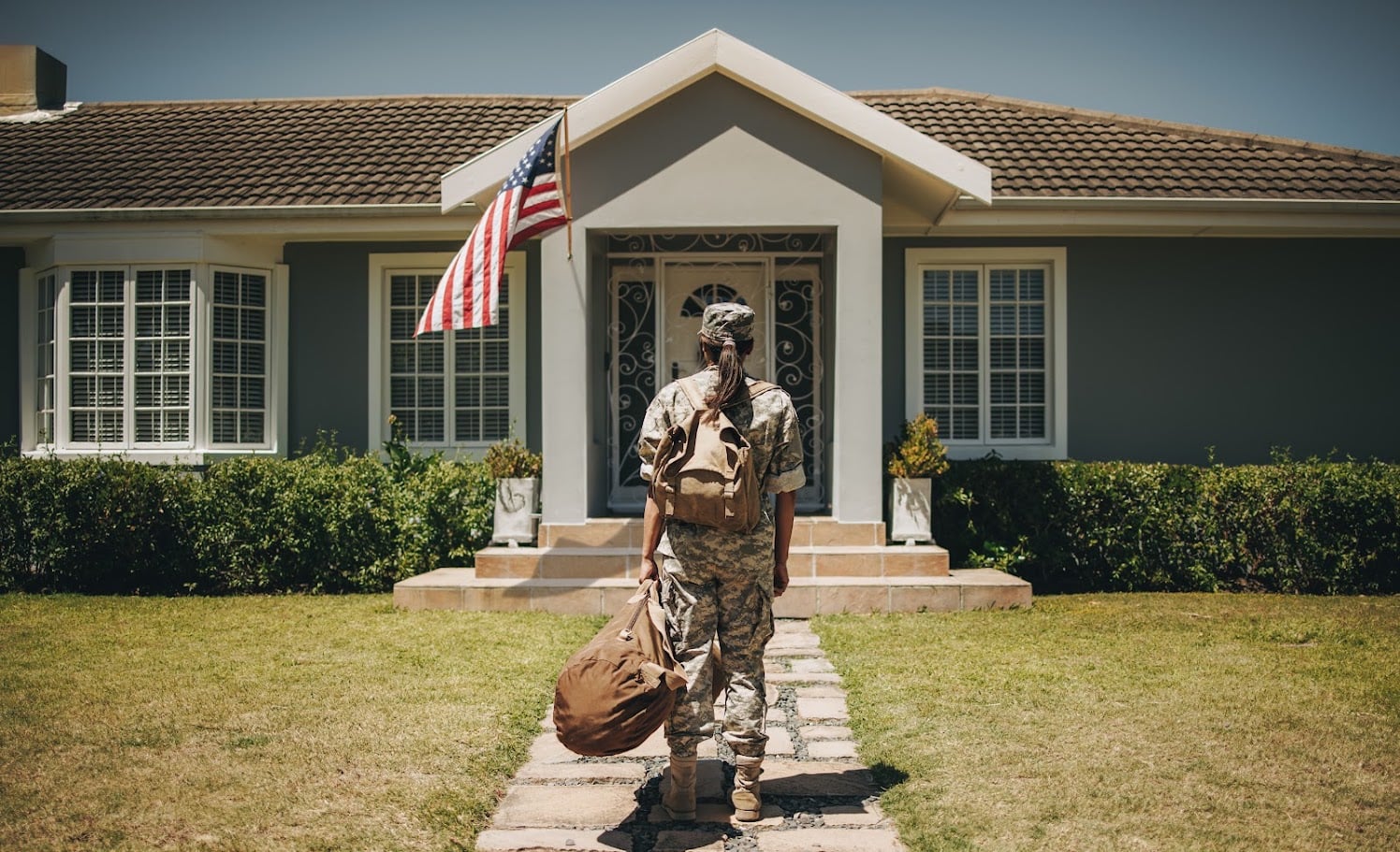 Rearview of a patriotic female soldier standing in front of her home with her luggage. Courageous servicewoman coming back home after serving her country in the military