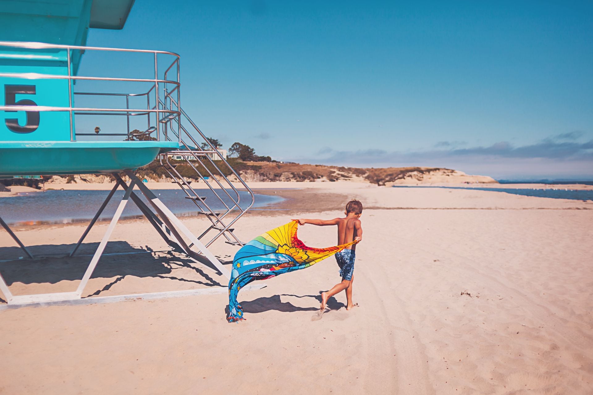 Boy running at the beach by a lifeguard tower
