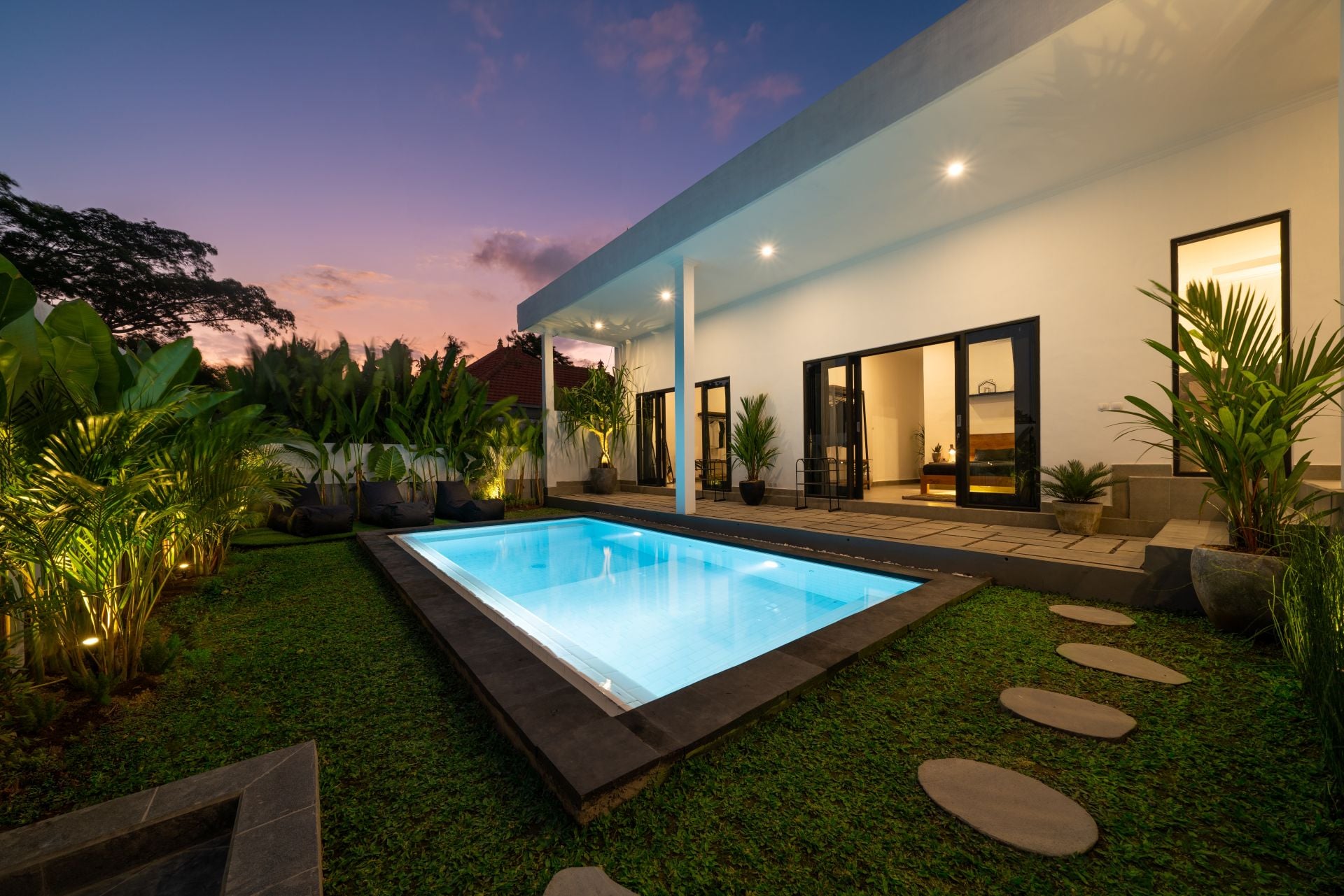Tropical villa view with garden, swimming pool and open living room at sunset. 1