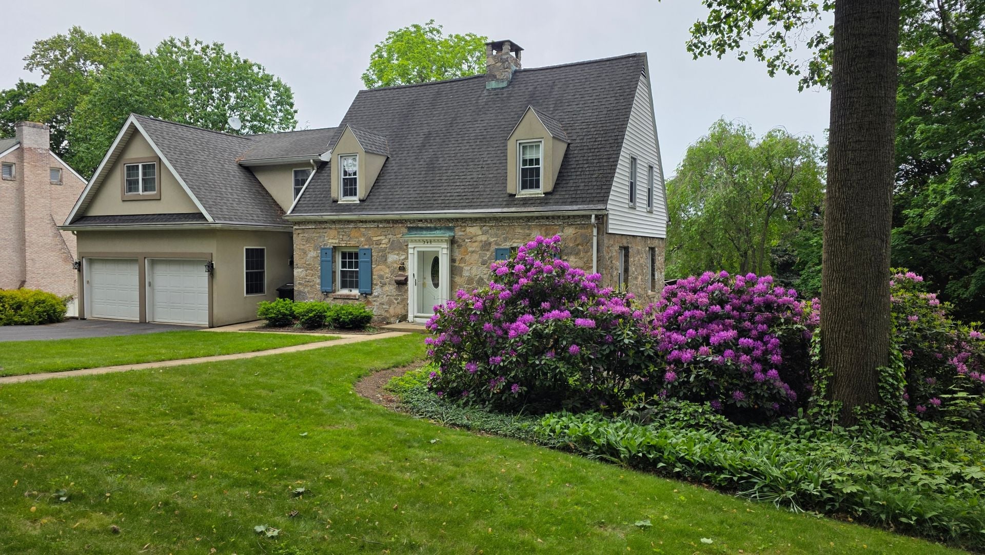 Middle class home in Pennsylvania built in the early 1900s with a stone exterior and blooming purple flowers in the front