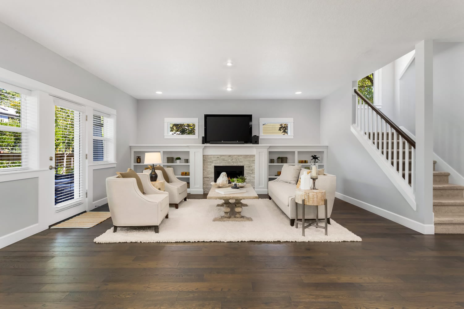 Beautiful living room in new traditional style home. Features fireplace, couch, coffee table, area rug, stairs, elegant furnishings, and door to backyard